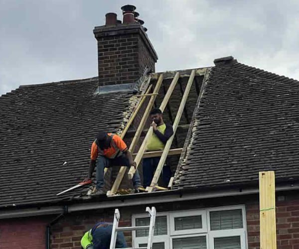 This is a photo of a roof repair being carried out. A section of the roof has been stripped and two roofers are replacing the rafters. Works being carried out by HJT Roofing Gainsborough